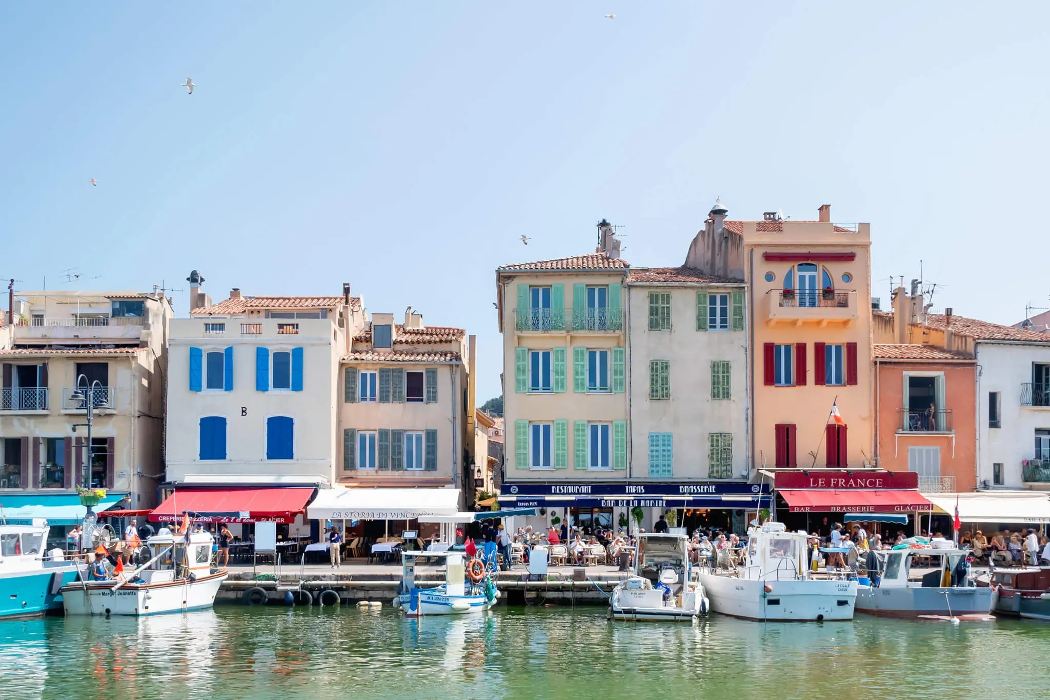 Vue imprenable sur la côte de Cassis avec une eau bleue cristalline et des bateaux colorés sous un ciel ensoleillé.