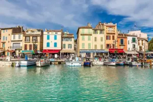 Port de pêche pittoresque de Cassis avec façades pastel colorées, bateaux en bois traditionnels, terrasses de café, falaises calcaires en arrière-plan et lumière dorée du coucher de soleil se reflétant sur l'eau calme.
