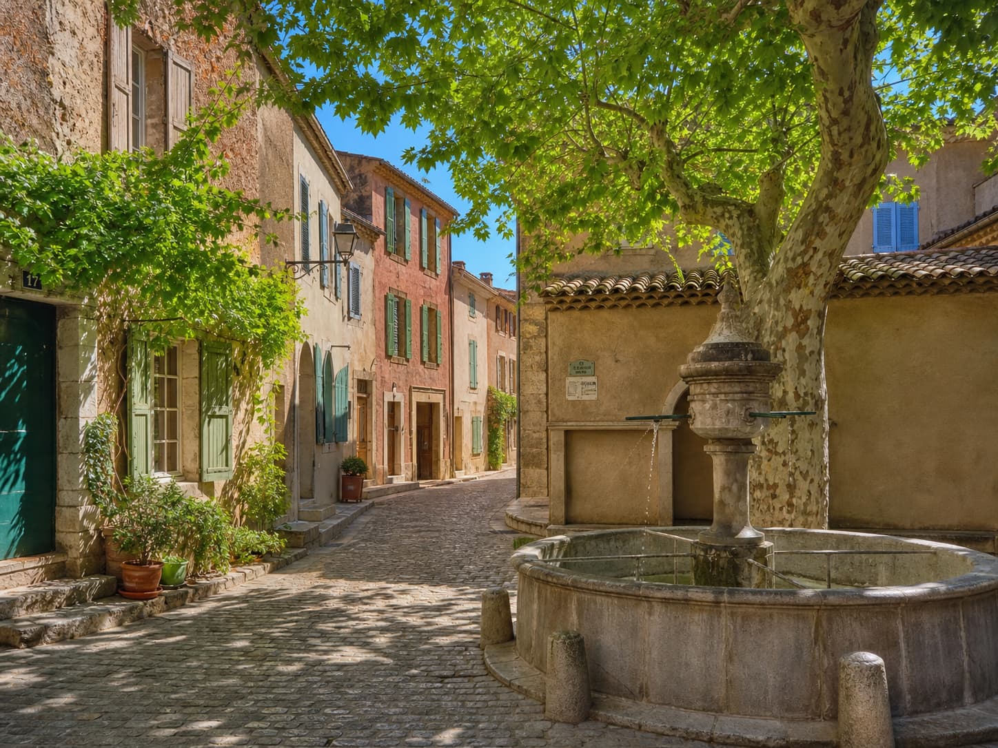 Rue pavée étroite avec maisons en pierre et volets colorés, une fontaine traditionnelle en pierre, éclairée par la lumière chaude de l