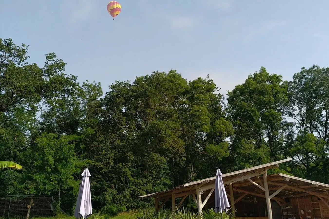 Vue aérienne du domaine Colline de Bouties à Labarthe avec trois cabanes, un gîte, une piscine turquoise, des transats, une aire de jeux et des chênes.